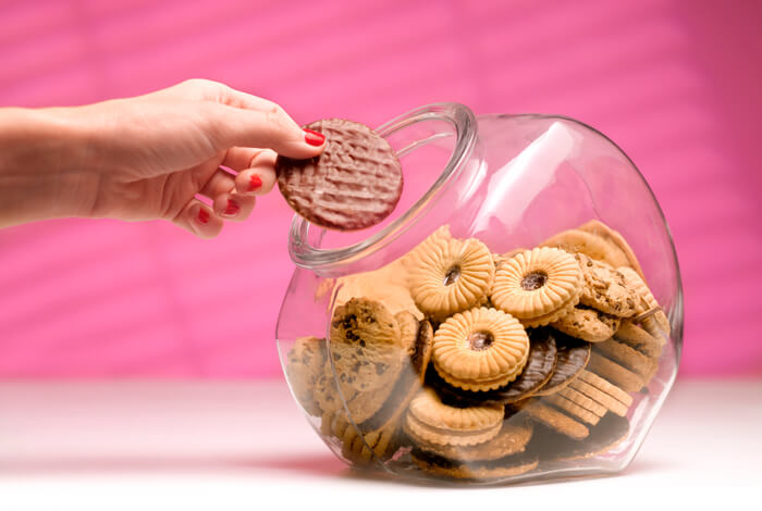 Hand reaching into a cookie jar and taking out a cookie.