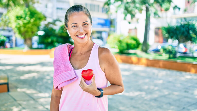 Smiling woman post-workout holding replica of heart.