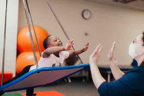 Child swinging on platform working with physical therapist